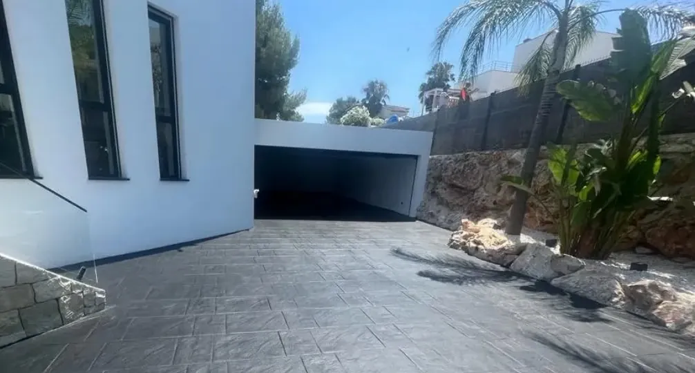 Entrada a un garaje en losa antracita, junto a una vivienda moderna con palmeras