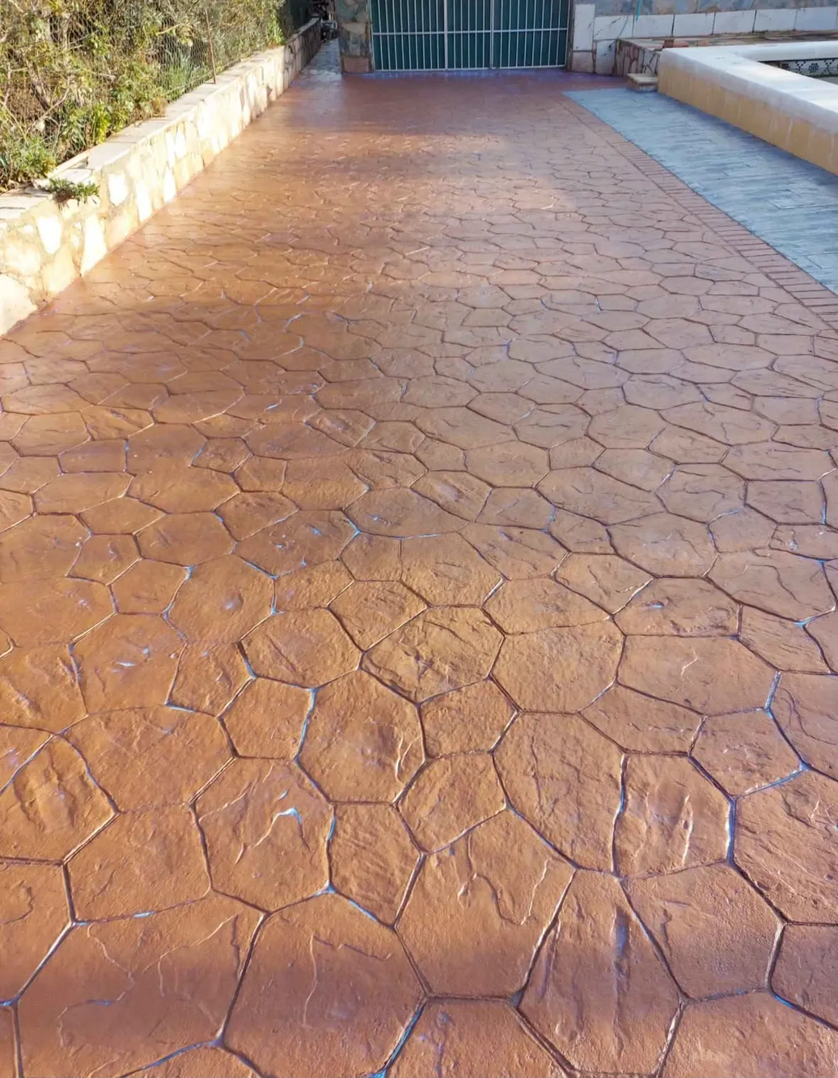 Entrada larga de hormigón impreso en piedra natural terracota junto a una piscina